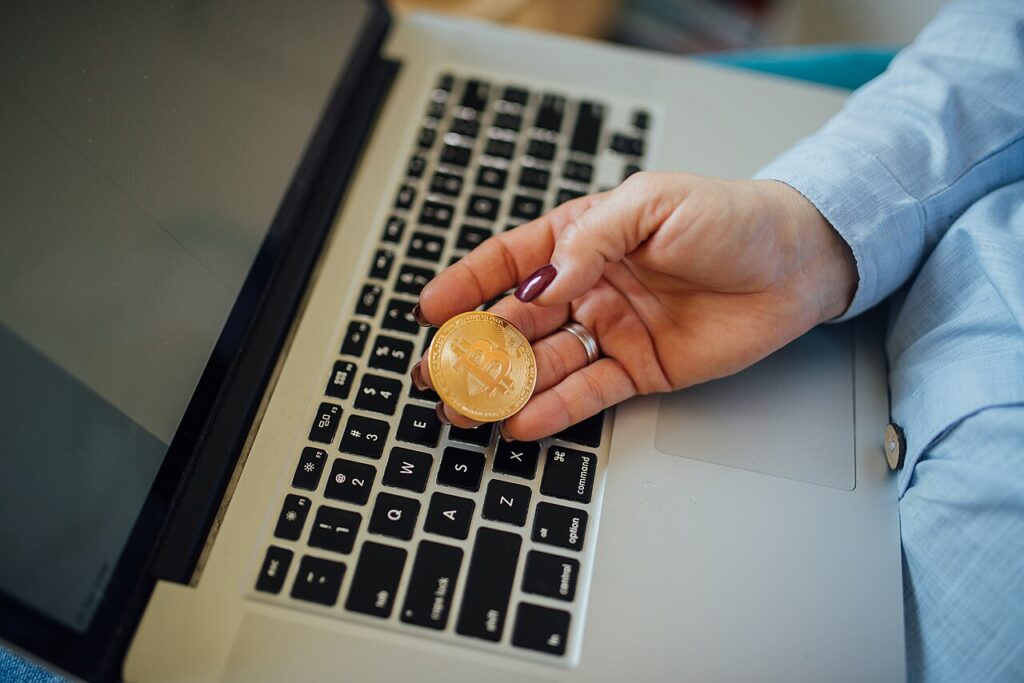 Airdrops crypto 2026 : comment repérer les vrais et éviter les arnaques Pièce de Bitcoin dans la main devant un ordinateur portable