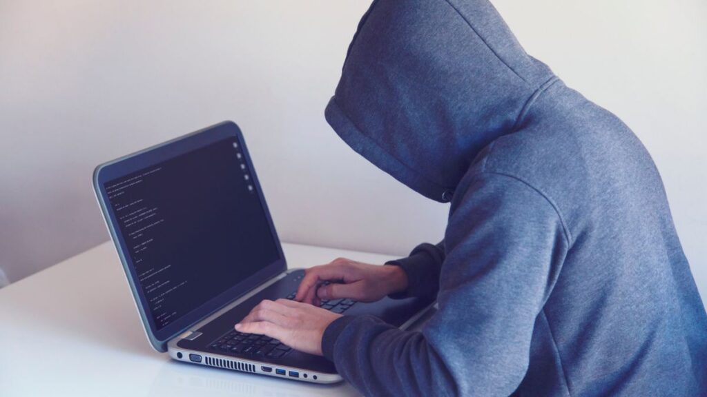 Arnaques en ligne en Afrique : ce que révèle l'opération Interpol Serengeti 2.0 (et comment te protéger) Pirate informatique encapuchonné devant un ordinateur